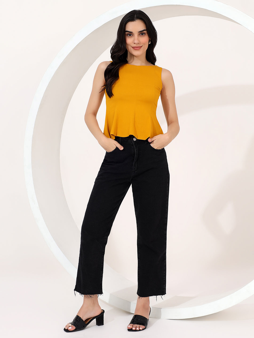 Woman wearing a mustard yellow top and black pants against a white background