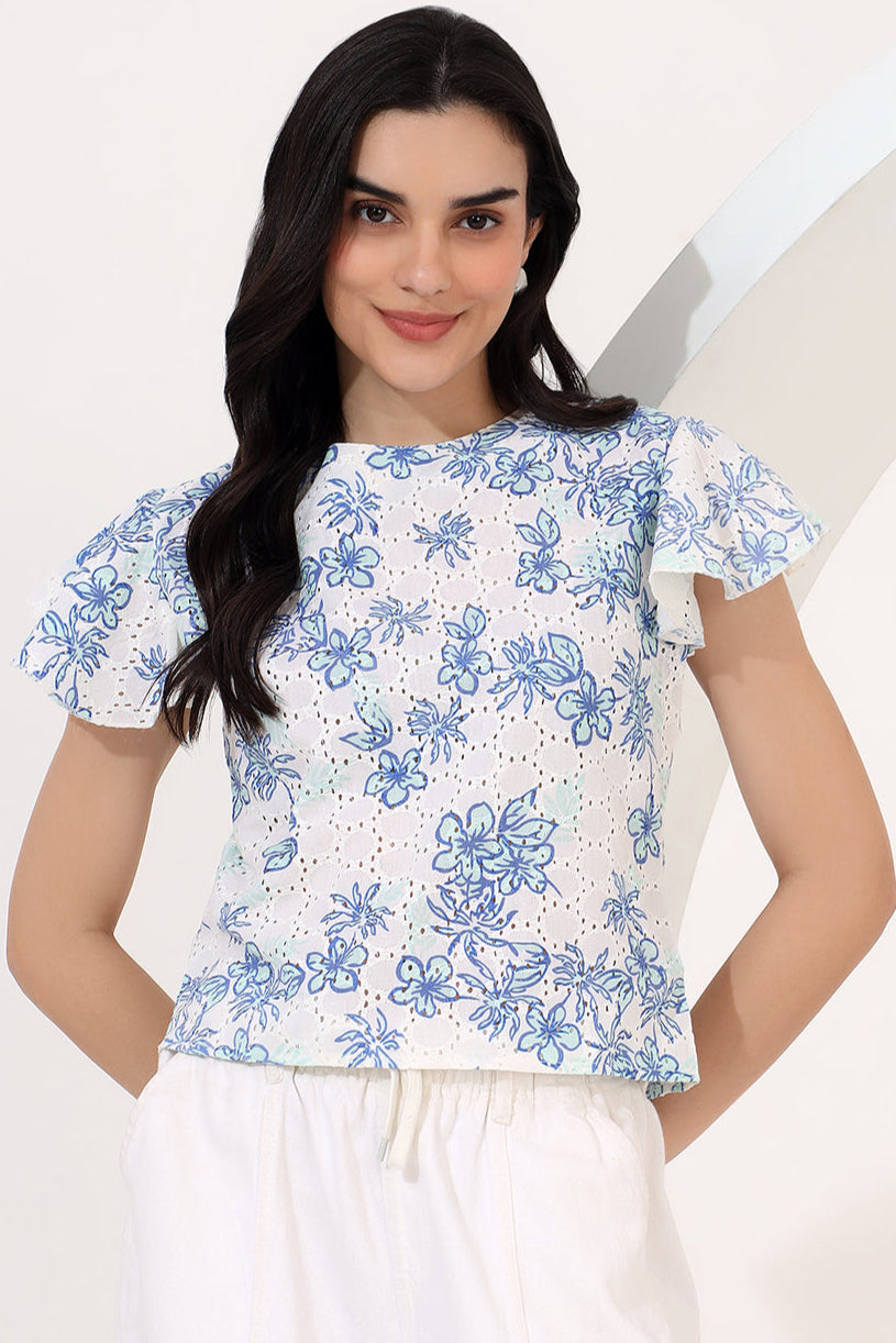 Woman wearing a white blouse with blue floral patterns on a plain background