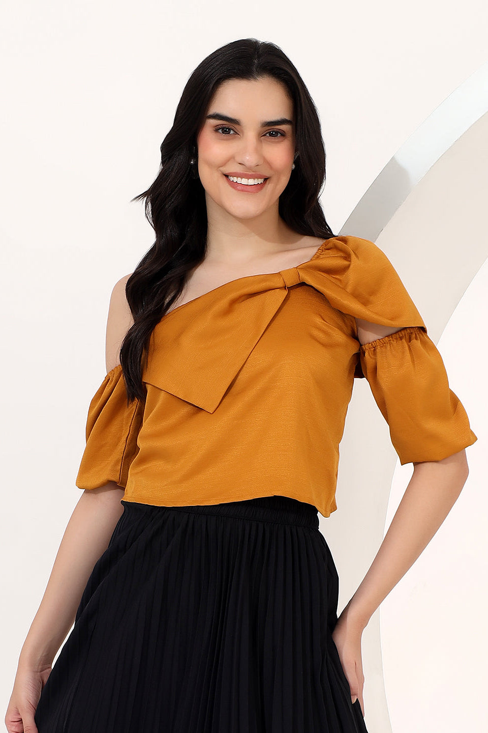 Woman wearing a mustard yellow top with a bow detail on a plain background