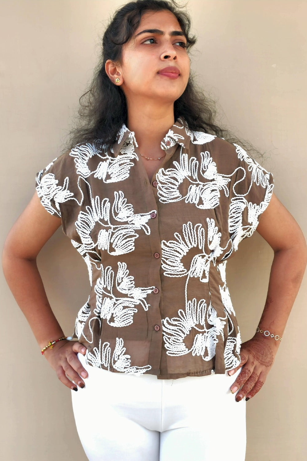 Woman wearing a brown shirt with white floral patterns against a plain background