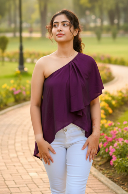 Woman in a purple top and white pants standing on a garden path with flowers and greenery.