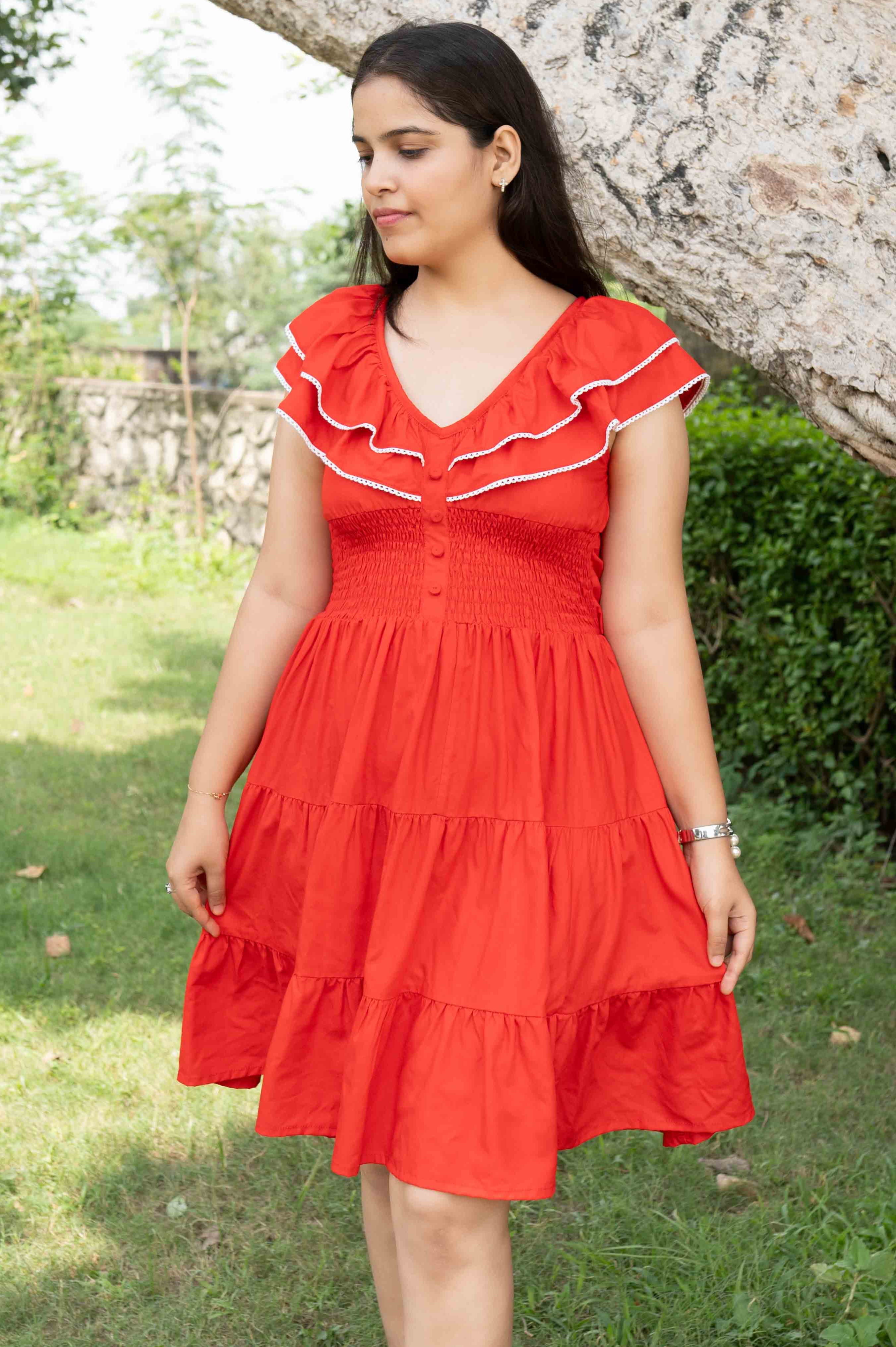 Woman wearing a red dress with white trim standing outdoors near a tree