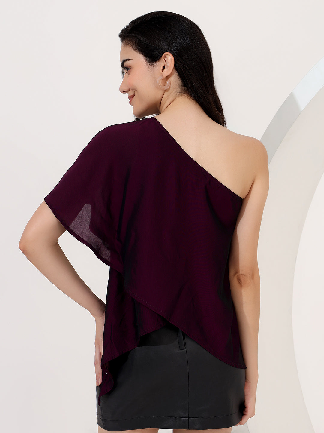 Woman wearing a one-shoulder burgundy top against a plain background