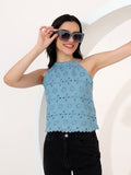 Woman wearing a light blue sleeveless top with a pattern, black sunglasses, and black pants against a white background.