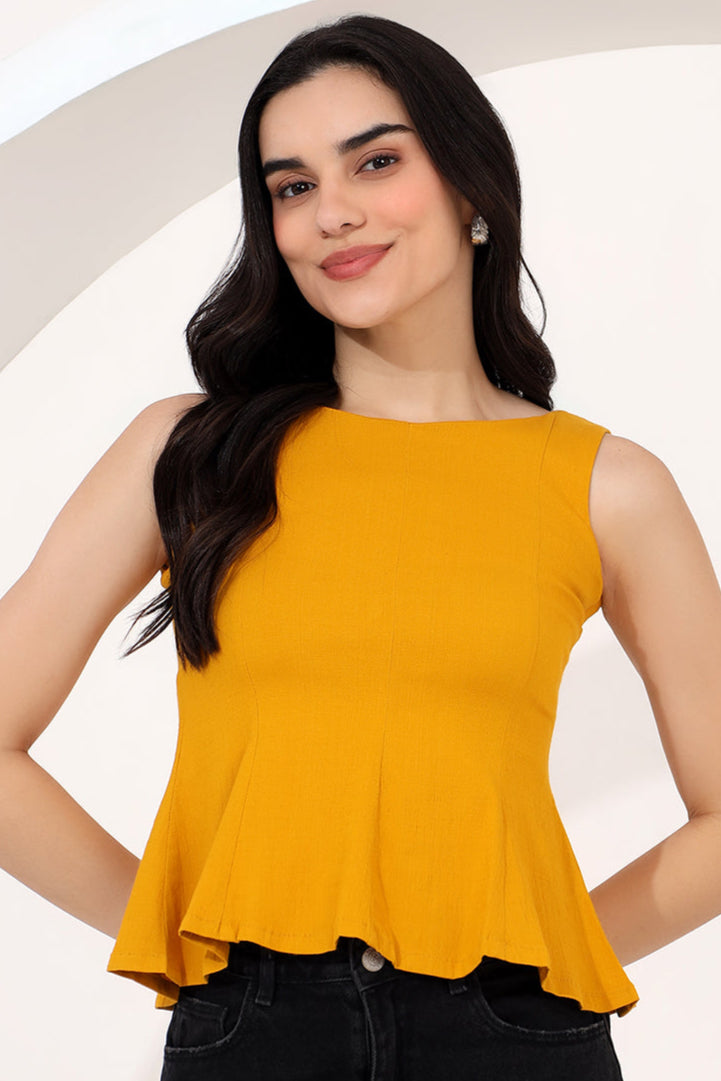 Woman in a yellow top and black pants standing on a cobbled street with buildings and people in the background.