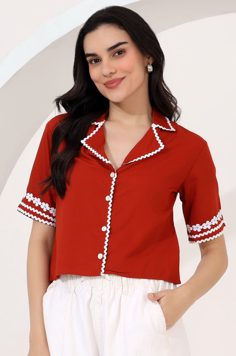 Woman in a red blouse and navy pants standing in an office setting with colleagues in the background.