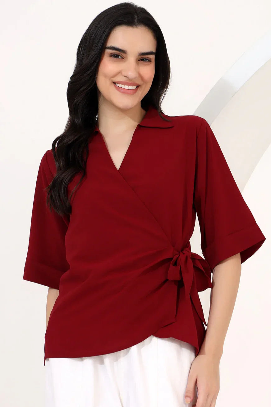 Woman in a red top and white pants standing on a path with modern buildings and palm trees in the background.