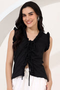 Woman wearing a black sleeveless top with ruffles and white pants on a light background