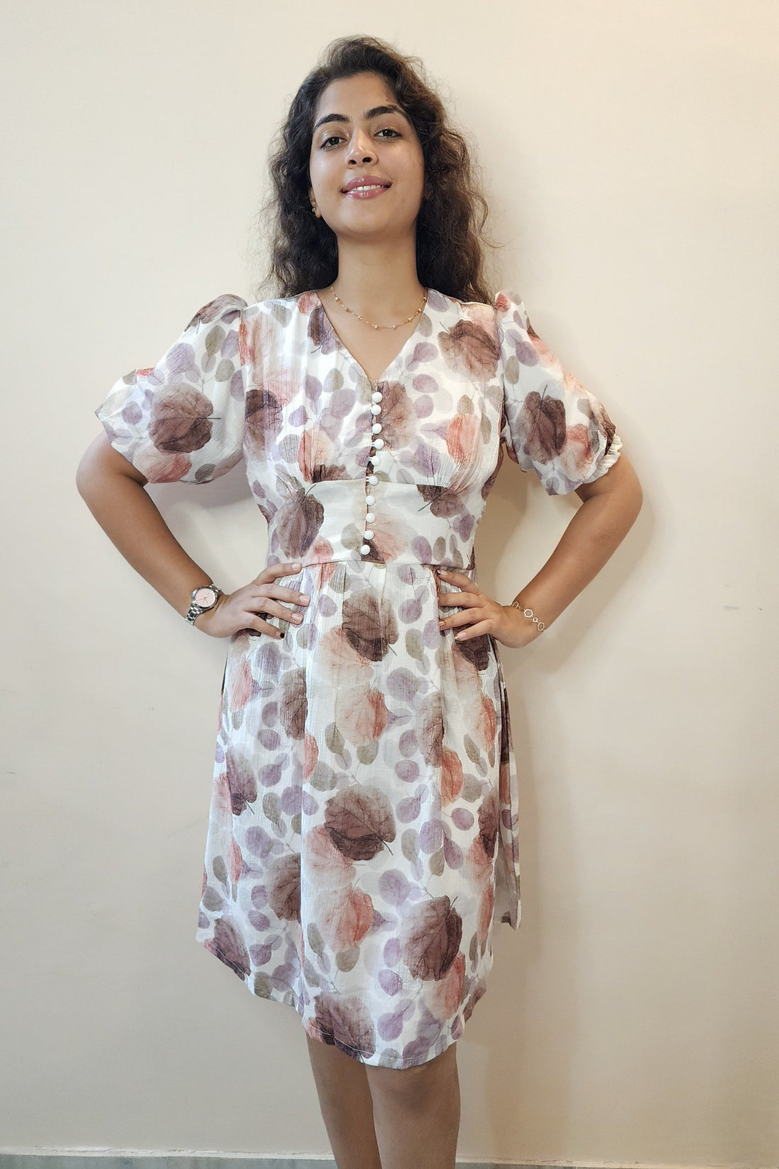 Woman in a floral dress standing on a sunlit street with buildings and ocean view.