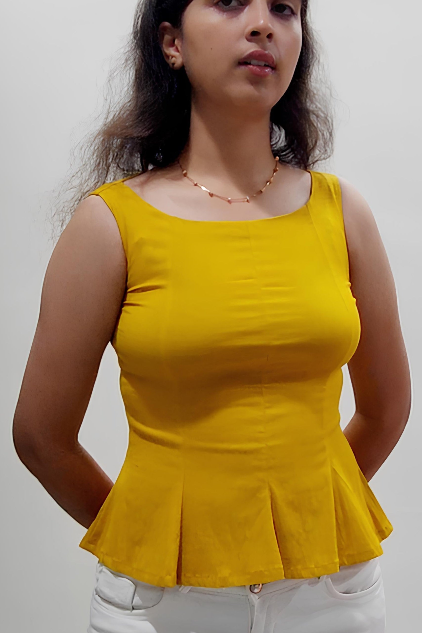 Woman wearing a yellow peplum top and white pants indoors.