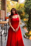 Woman in a red dress standing outdoors with trees and a building in the background