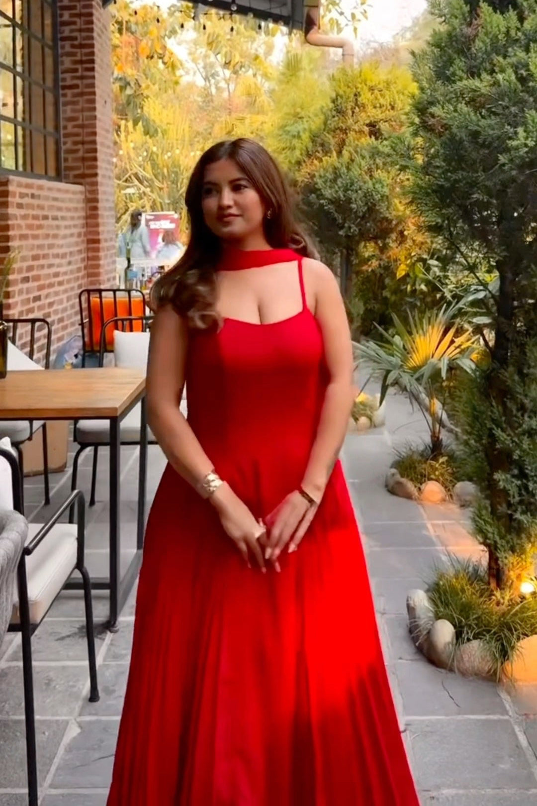 Woman in a red dress standing outdoors with trees and a building in the background