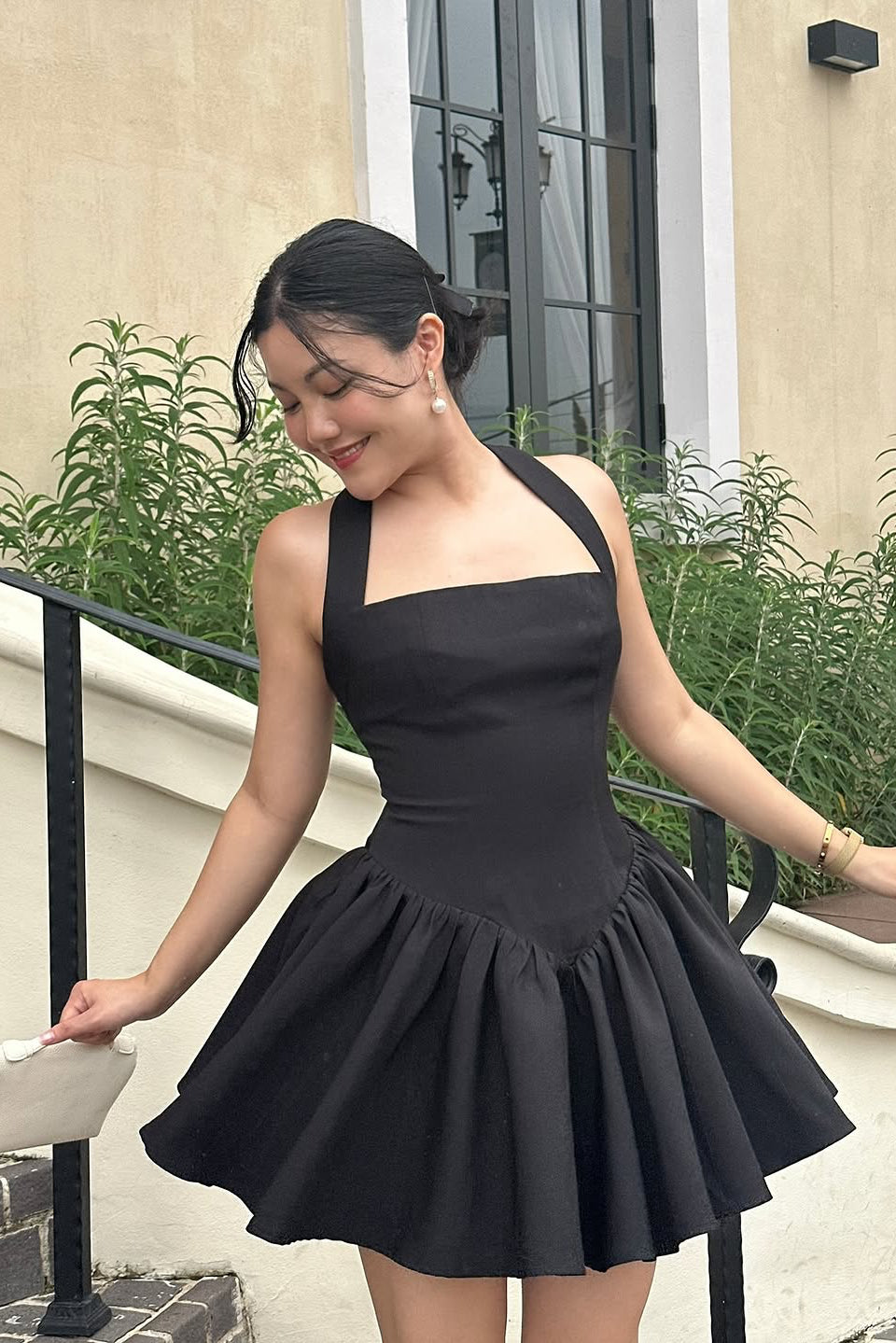 Woman wearing a black dress standing outdoors near a building with plants.