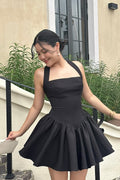 Woman wearing a black dress standing outdoors near a building with plants.