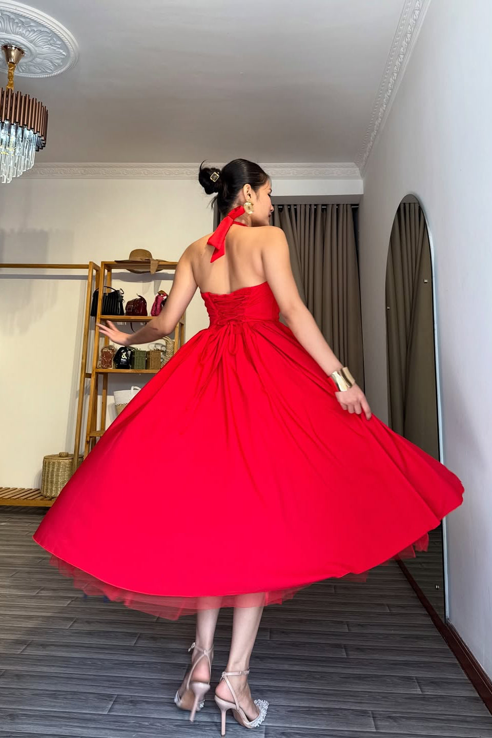 Woman in a red dress standing in a room with a wooden floor and shelves.