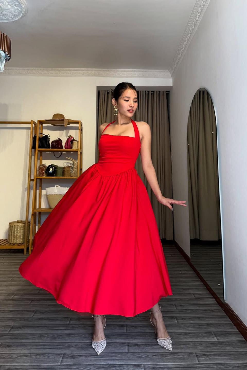 Woman in a red dress standing in a room with a wooden floor and shelves.