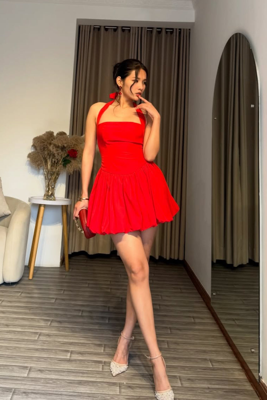 Woman in a red dress standing in a room with a couch and curtains.