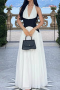 Woman in a black and white dress holding a black handbag in an outdoor setting with greenery and a building in the background.