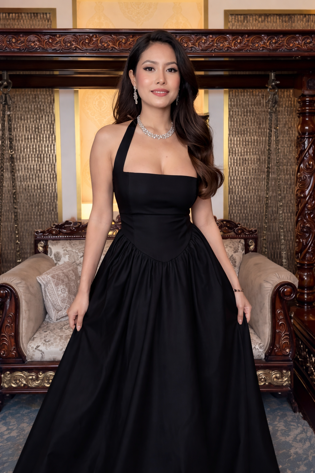 Woman in a black evening gown standing in an elegant room with ornate furniture.