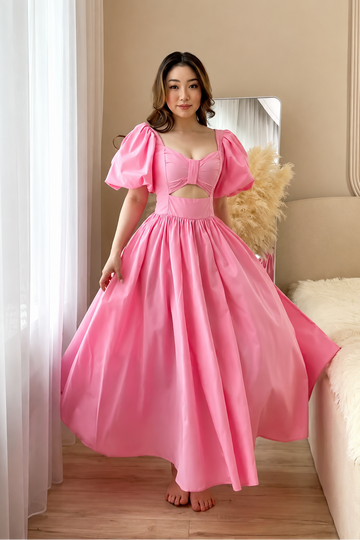 Woman in a pink dress standing in a room with a mirror and decorative elements.