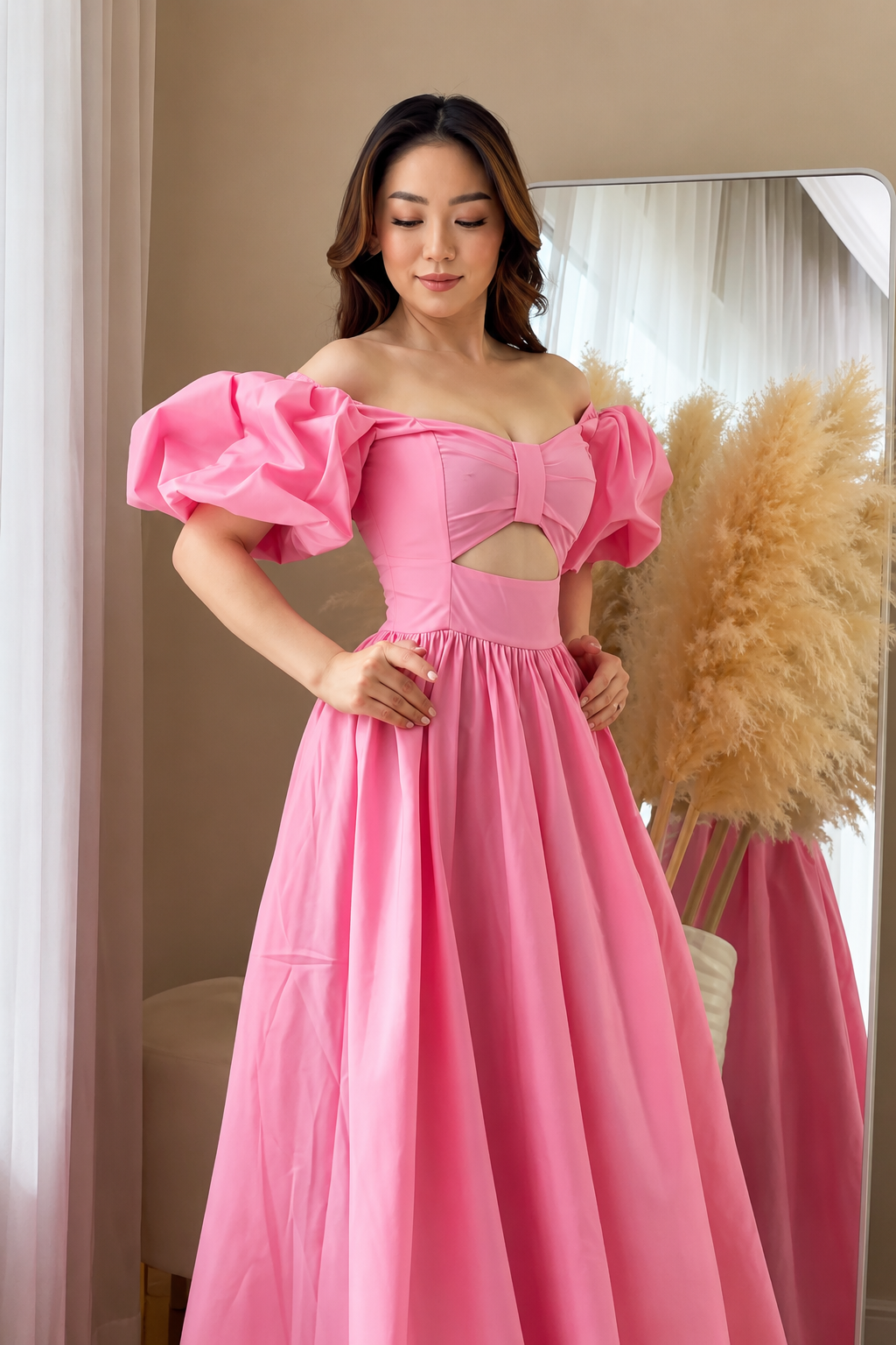Woman in a pink dress standing in a room with a mirror and decorative elements.