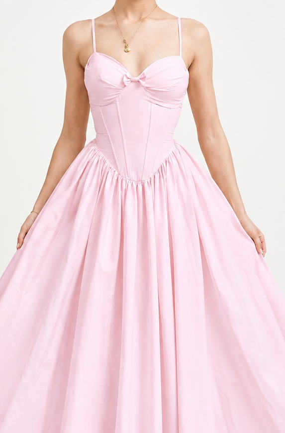 A woman modeling a light pink strapless midi dress with a sweetheart neckline, fitted corset-style bodice, and a full flared skirt, photographed against a plain light gray studio background.