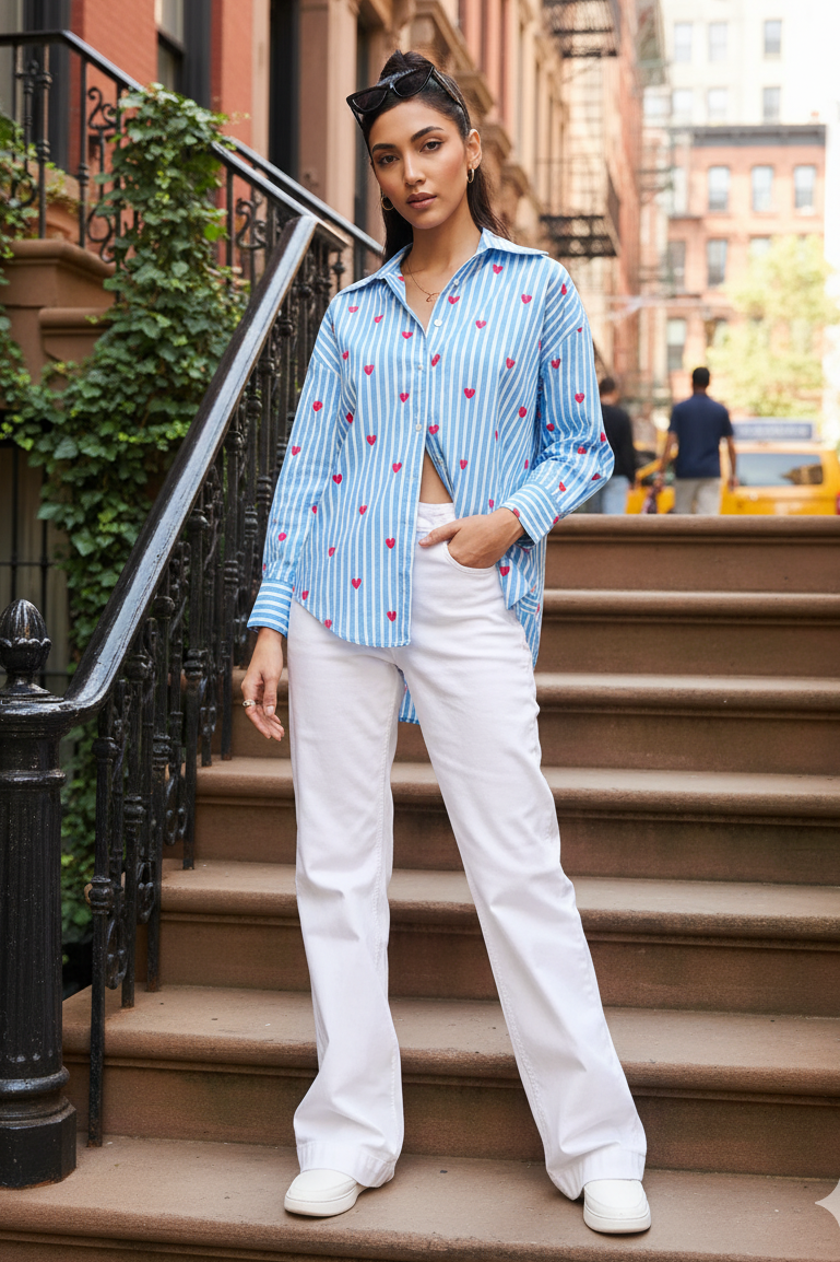 Woman in a blue patterned shirt and white pants standing on a city street.