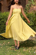 Woman in a yellow strapless dress standing outdoors with greenery in the background