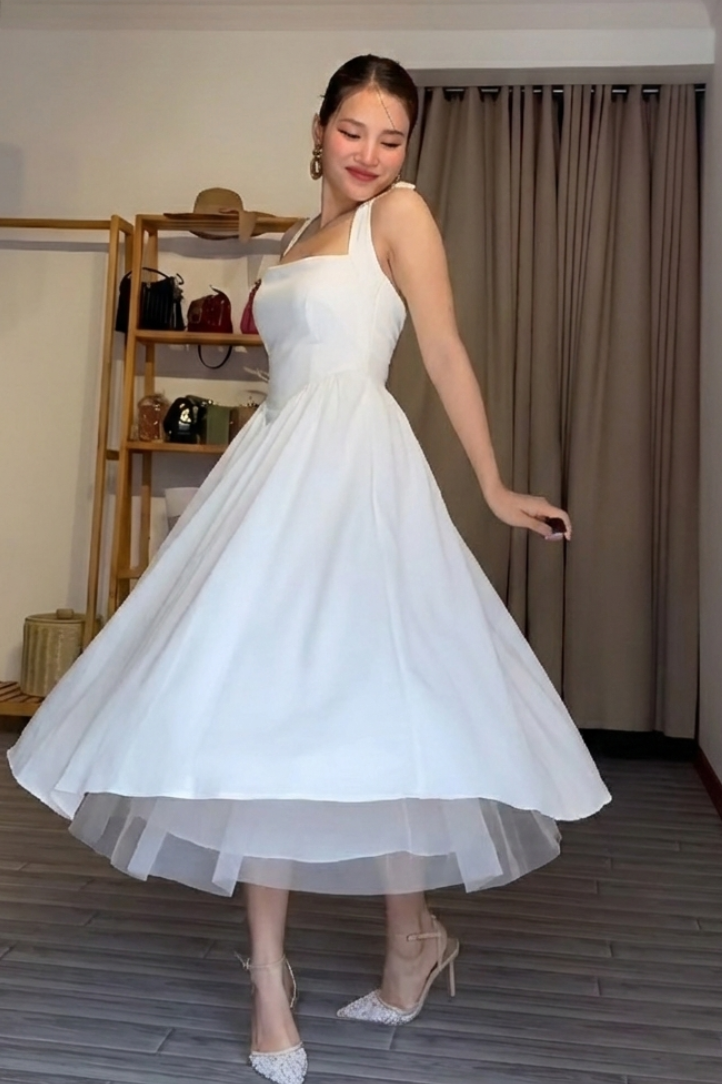 Woman in a white dress posing in a room with a neutral color scheme.