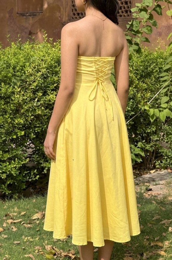 Woman in a yellow dress standing in a garden with a historical building in the background