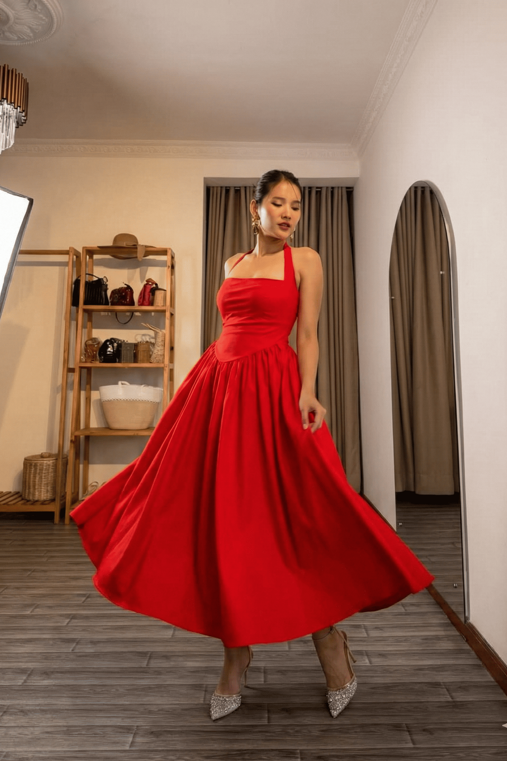 Woman in a red dress standing in a room with wooden floor and shelves.