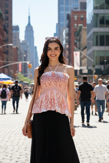 Woman in a pink top and black skirt standing on a city street with tall buildings in the background.