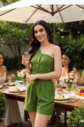 Woman in a green dress holding a glass of wine at an outdoor dining table with friends.
