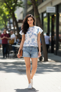 Woman wearing a floral top and denim shorts walking on a sidewalk.