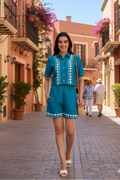 Woman in a blue outfit walking down a sunlit street with buildings and plants.