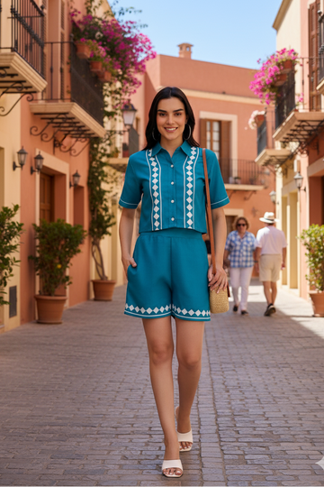 Woman in a blue outfit walking down a sunlit street with buildings and plants.