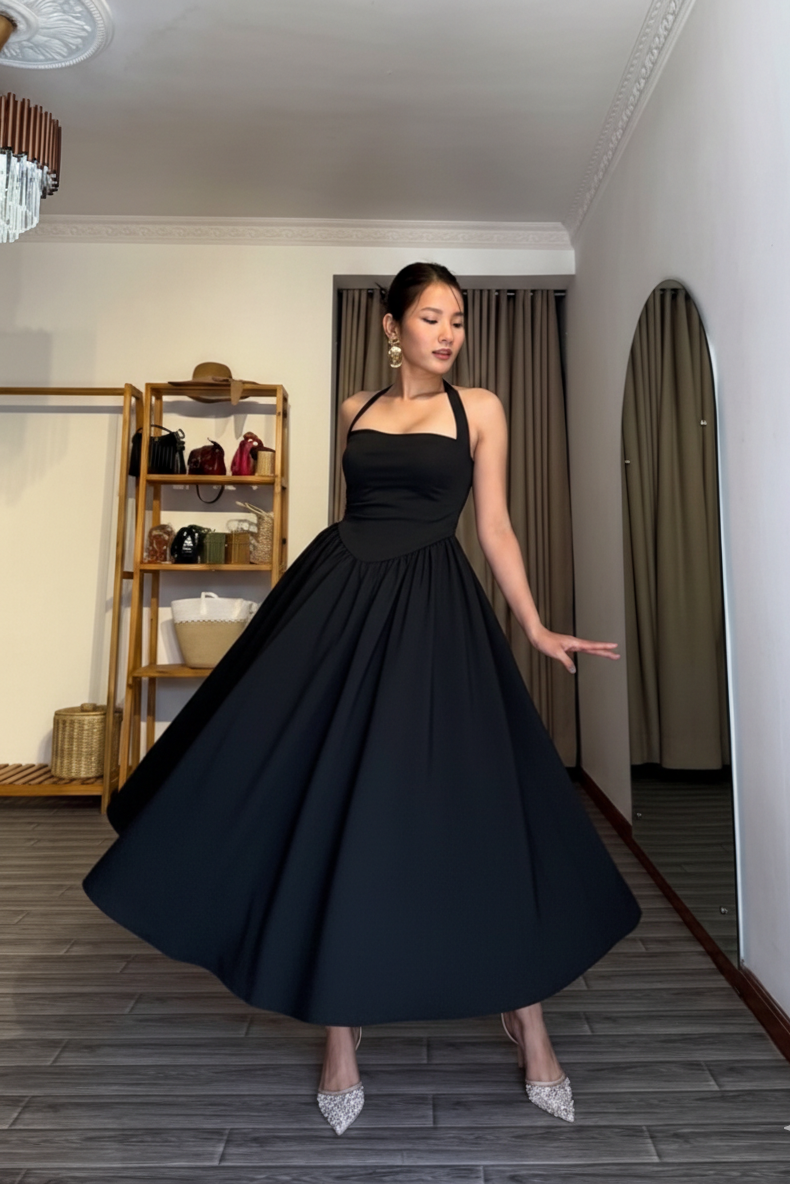 Woman in a black dress standing in a room with a mirror and shelves.