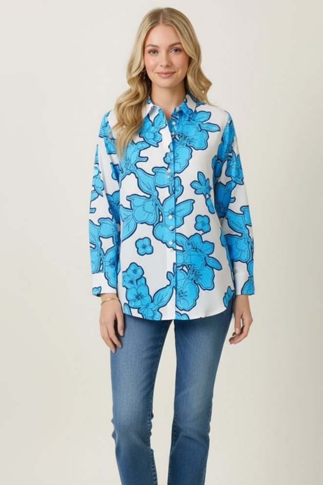 Woman in a blue floral shirt and jeans standing on stone steps with traditional architecture in the background.