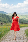 Woman in a red dress standing on a stone path with green hills and blue sky in the background