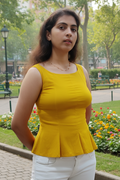 Woman wearing a yellow top and white pants standing in a park.