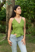 Woman wearing a green top and blue jeans standing outdoors with trees in the background