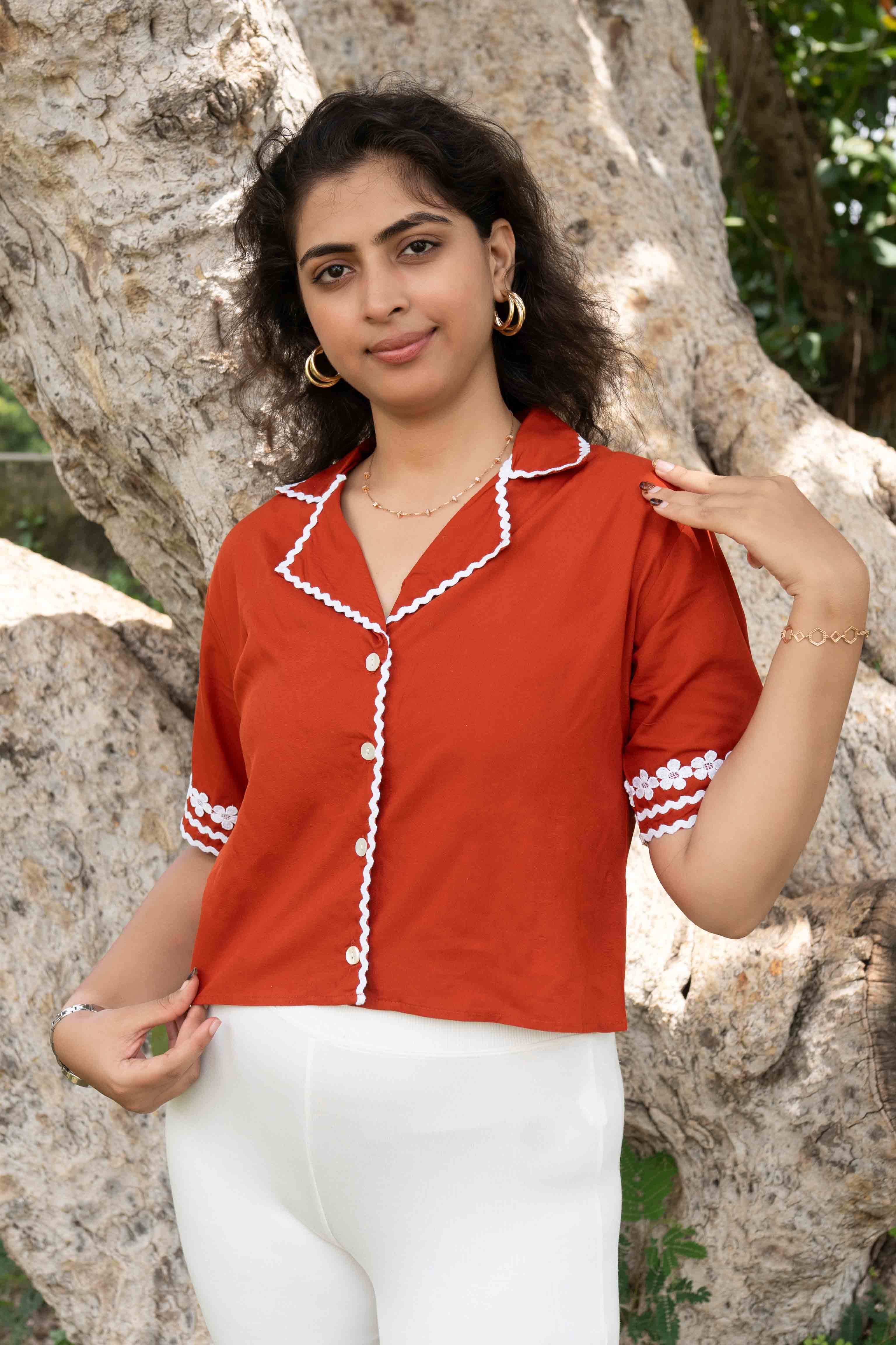 Woman wearing a red blouse with white trim standing in front of a tree