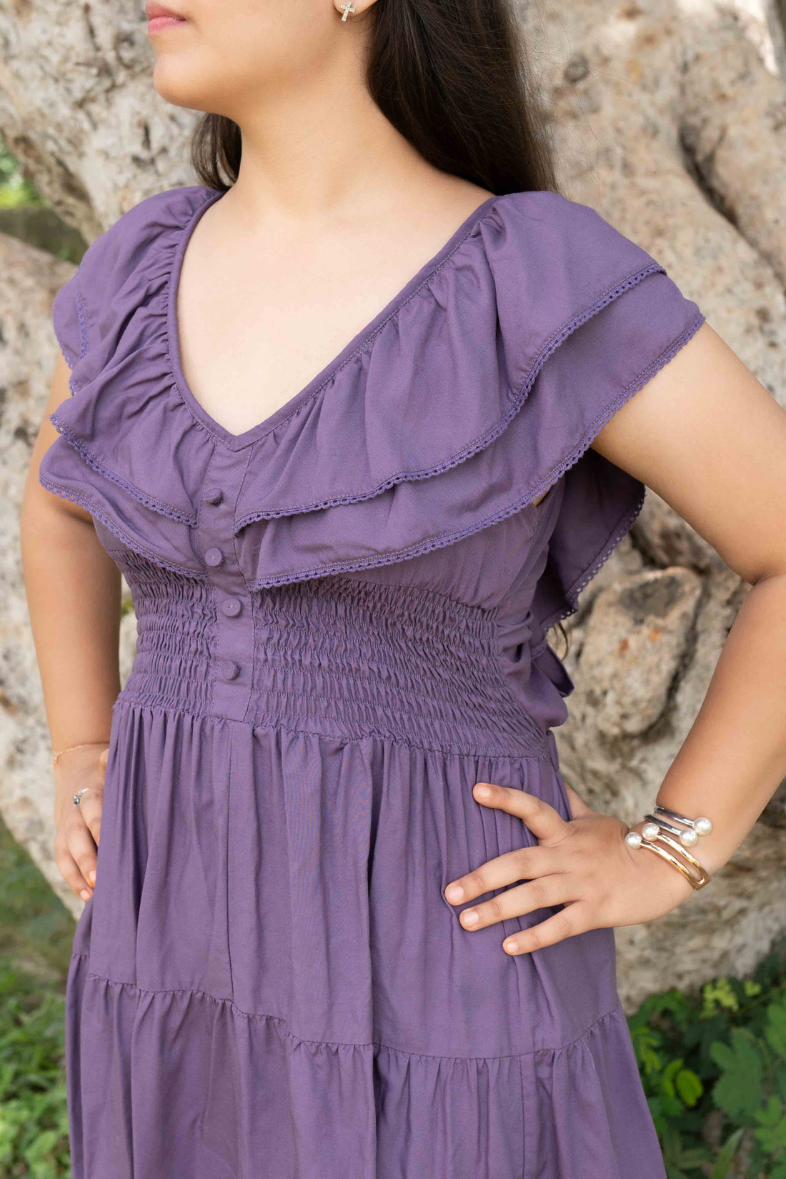 Woman in a purple dress standing in a garden with floral decorations and people in the background.