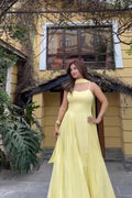 Woman in a yellow dress standing in front of a yellow building with a window.