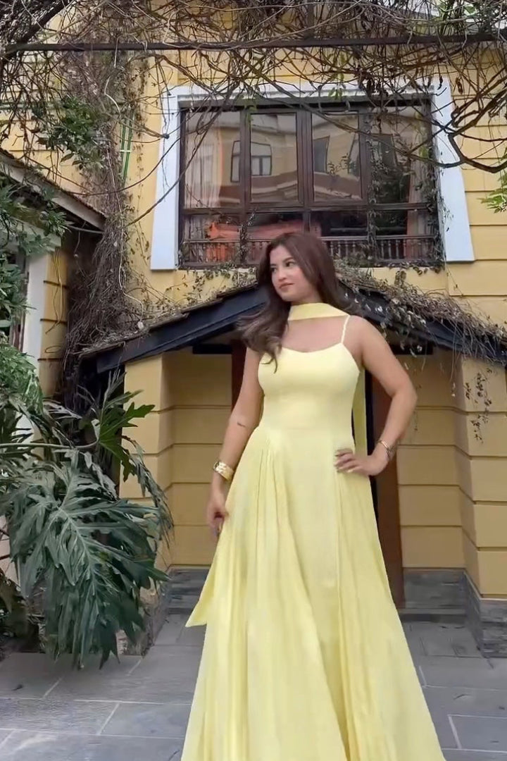 Woman in a yellow dress standing in front of a yellow building with a window.
