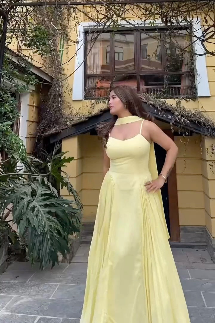 Woman in a yellow dress standing outdoors near a building with a window.