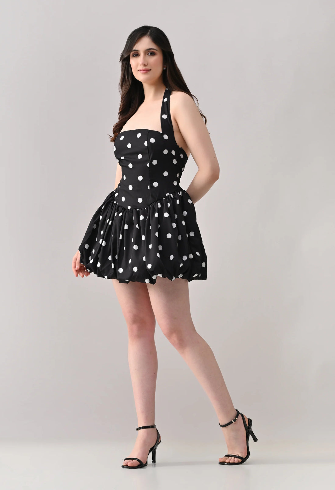 Woman wearing a black dress with white polka dots on a gray background