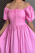 Woman wearing a pink off-shoulder dress with puff sleeves.