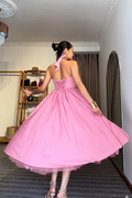 Woman in a pink dress standing in a room with a mirror and shelves.