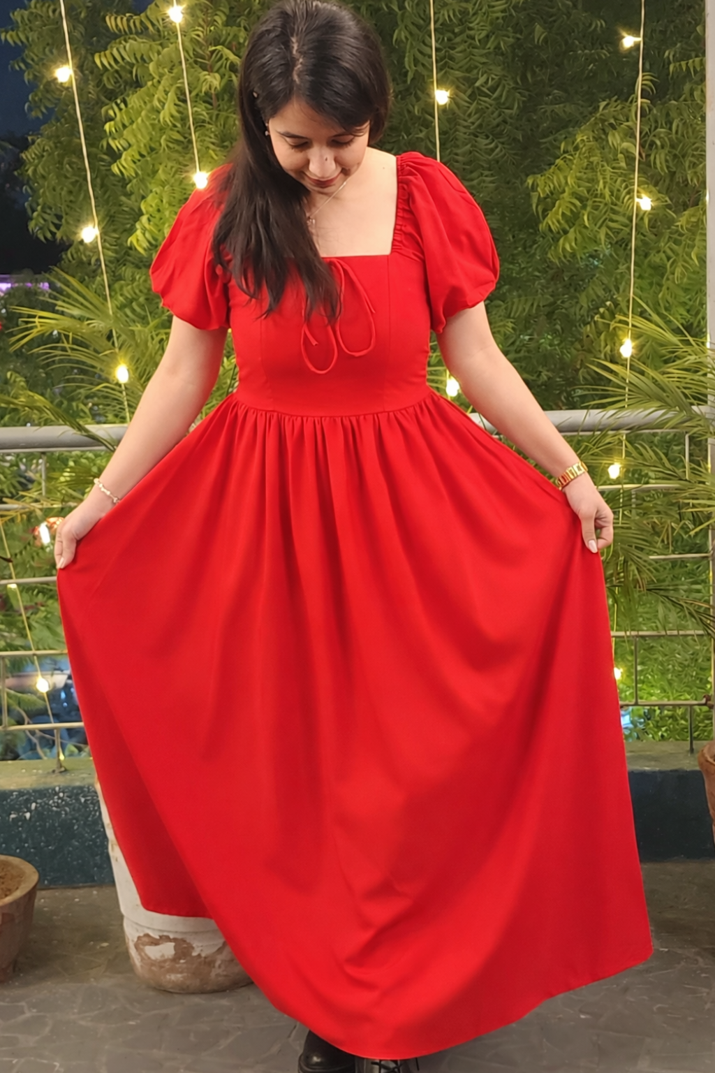Woman wearing a red dress standing outdoors with greenery in the background